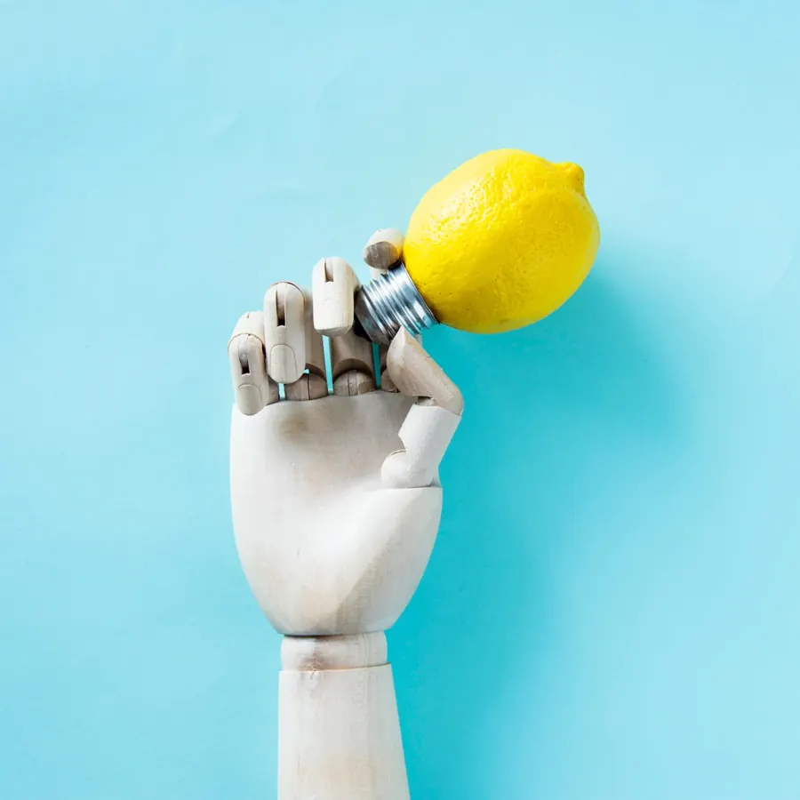 A wooden hand holding a light bulb made from a lemon, on a pale blue background